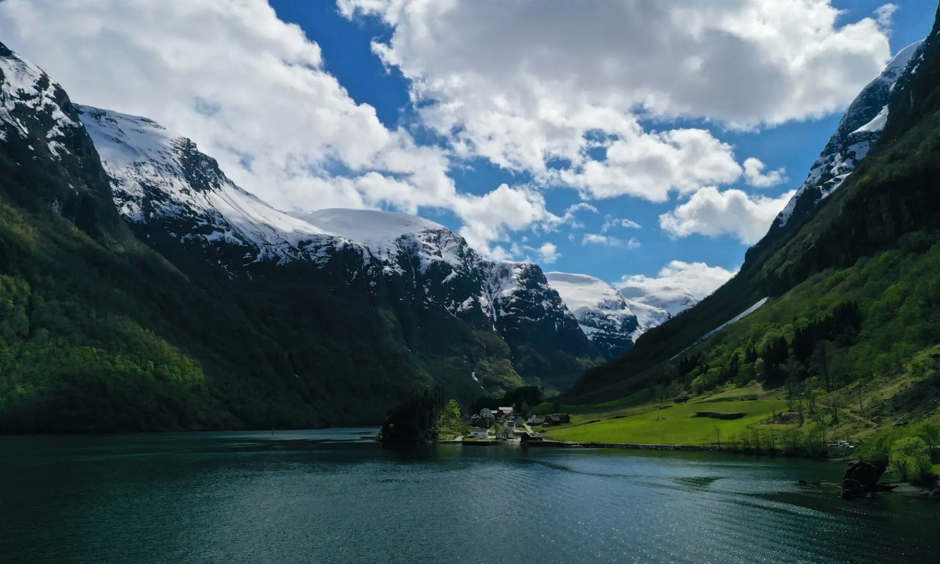Norsk fjordlandskab med sneklædte bjerge, grønne skråninger og stille vand